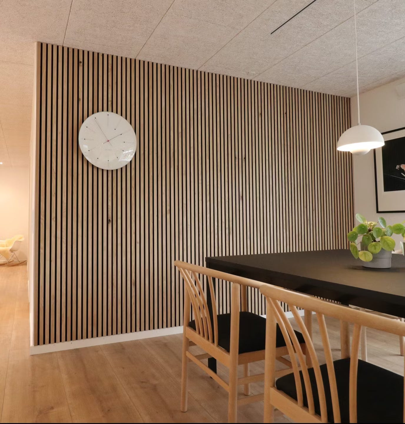 Comedor moderno con una pared de acento nórdico de lamas de madera acústica Akupanel, mesa negra, sillas de madera con asientos negros y un centro de mesa con una maceta.