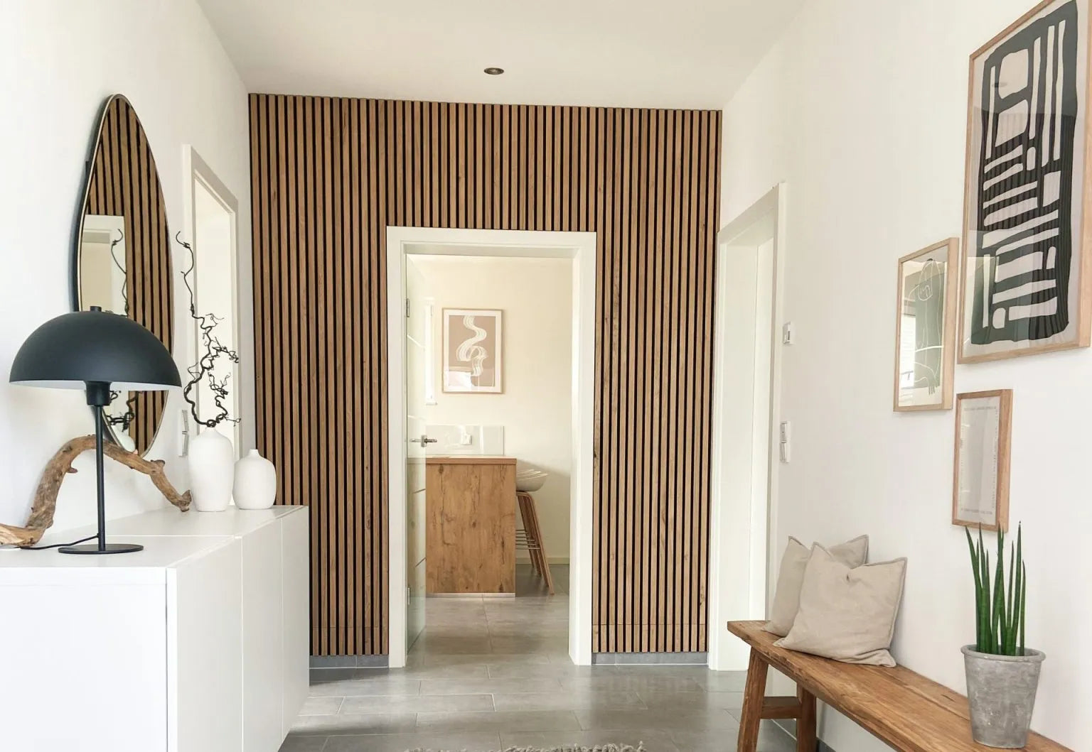 Un pasillo moderno con una pared de acento acústico de lamas de madera nórdica Akupanel, paredes blancas, un banco acolchado y decoración minimalista.
