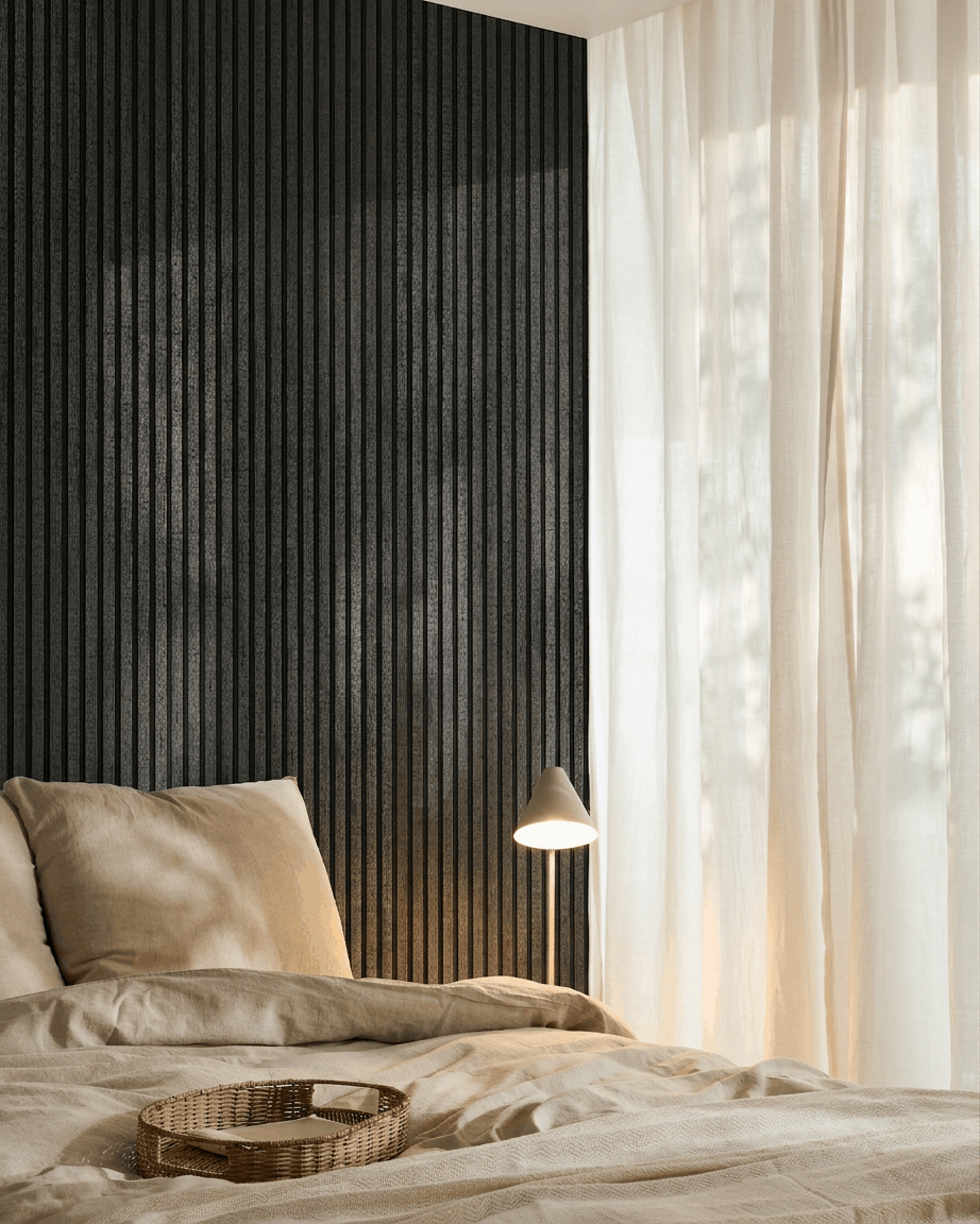 Dormitorio acogedor con ropa de cama beige, una bandeja de ratán, una lámpara blanca, cortinas vaporosas y un panel acústico de madera WoodUpp Akupanel en charcoal montado en la pared.