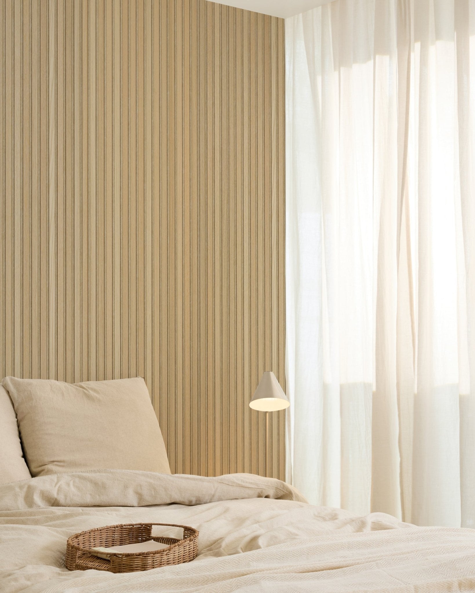 Dormitorio minimalista con ropa de cama beige, una bandeja de mimbre, un aplique de pared moderno, una pared decorativa de panel acústico de madera Akupanel y cortinas translúcidas que filtran una luz natural suave.