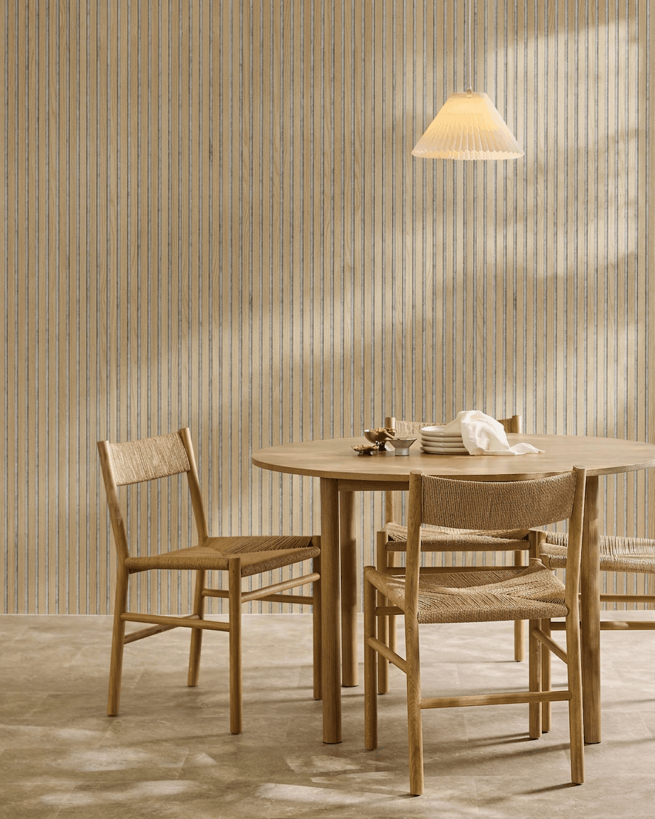 Comedor minimalista con una mesa redonda de madera, sillas tejidas, una lámpara colgante y un panel acústico de madera WoodUpp Akupanel en Classic Oak con fieltro grey.