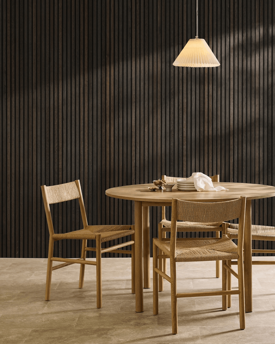 Comedor minimalista con una mesa de madera, sillas escandinavas, lámpara colgante y un panel acústico de listones WoodUpp Akupanel Rustic Smoked Oak.
