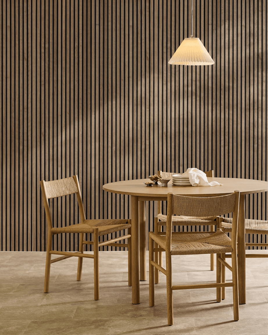 Comedor minimalista con mesa redonda, sillas de mimbre, lámpara colgante y un panel acústico de madera WoodUpp Akupanel en Natural Wood con fieltro black en la pared.