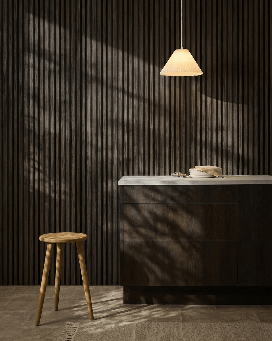 Cocina minimalista con paneles acústicos WoodUpp Akupanel Black Oak en la pared, taburete de madera, encimera blanca, lámpara colgante beige y sombras iluminadas por el sol.