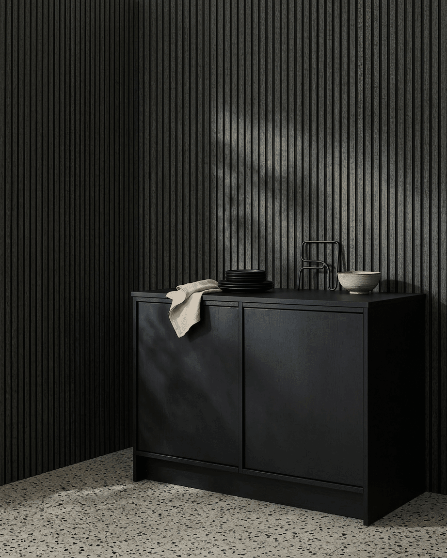 Un mueble black junto a un panel acústico de madera WoodUpp Akupanel en Charcoal/Black Felt, con cuencos y platos encima, sobre un suelo de terrazo claro.