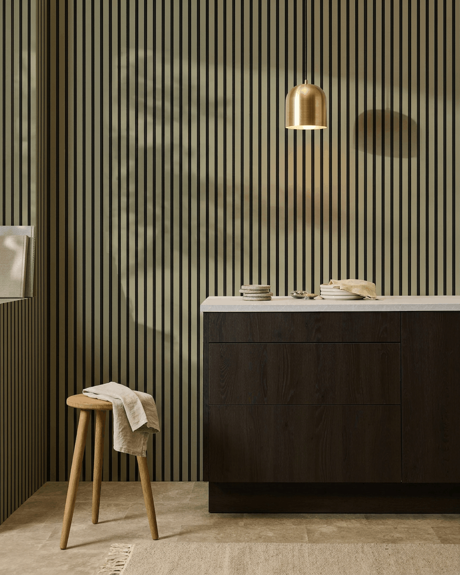 Cocina moderna con armarios de madera oscura, encimera de mármol, lámpara colgante brass y un panel de pared de listones acústicos WoodUpp Akupanel Colored para la absorción del sonido.