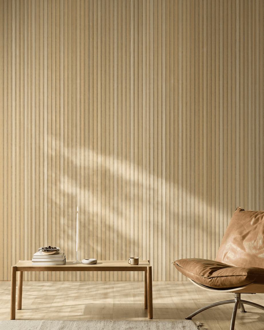 Espacio escandinavo minimalista con un panel acústico de madera WoodUpp Akupanel en Roble Clásico Natural Wood, una silla de cuero color canela y una mesa sencilla de madera con detalles acogedores.