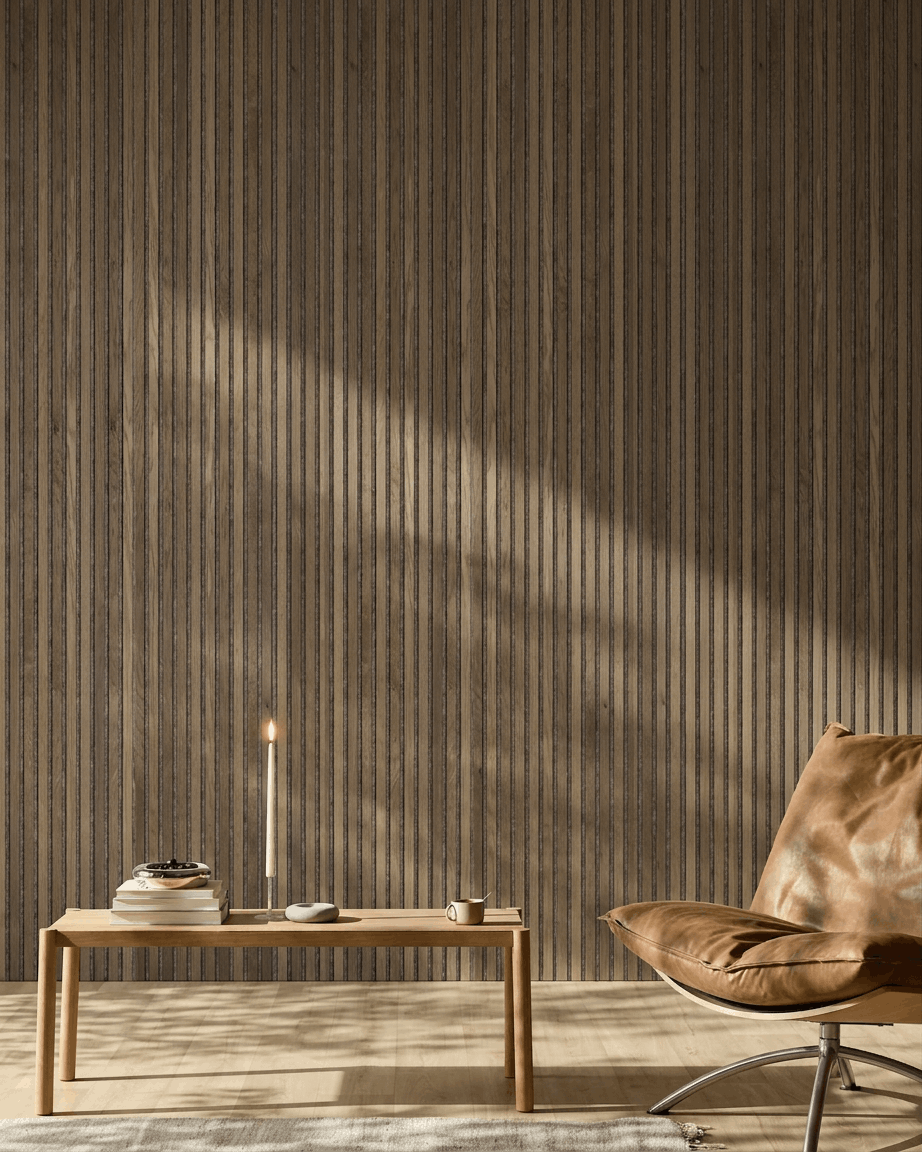 Una estancia moderna con una silla de cuero brown, una mesa de madera y un WoodUpp Akupanel en Rustic Grey Oak montado en la pared, iluminado por una suave luz natural.