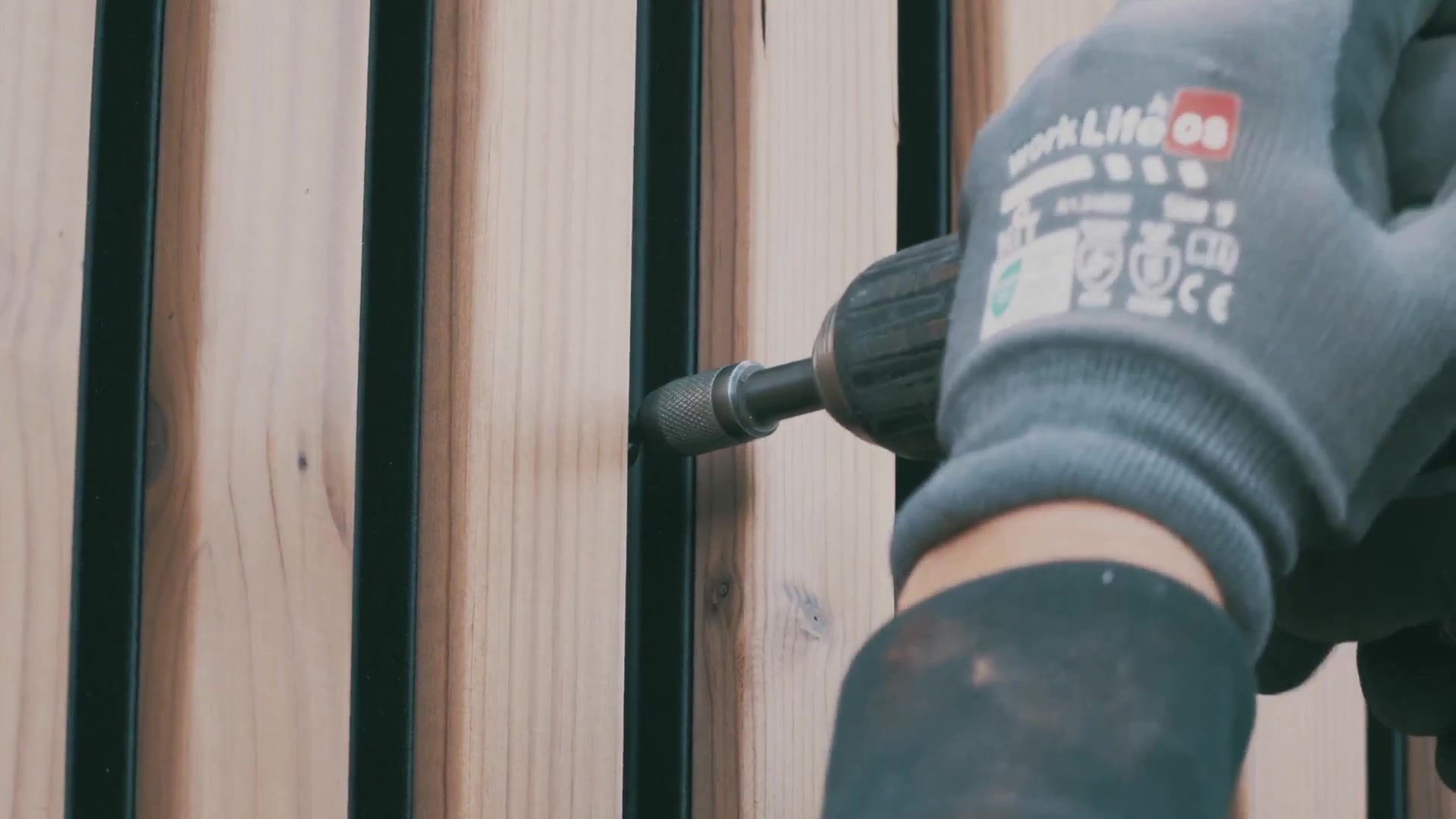 Gloved hand driving a screw through the rail between vertical Aluwood slats