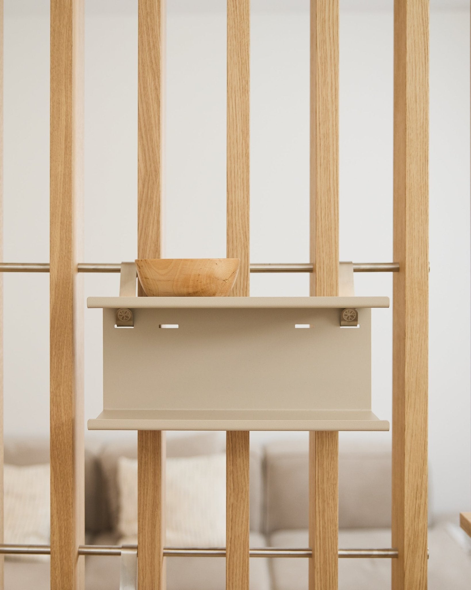 Un cuenco de madera small sobre la estantería Nell Double Metal beige de WoodUpp (31.7 cm), con un sofá y cojines desenfocados al fondo.
