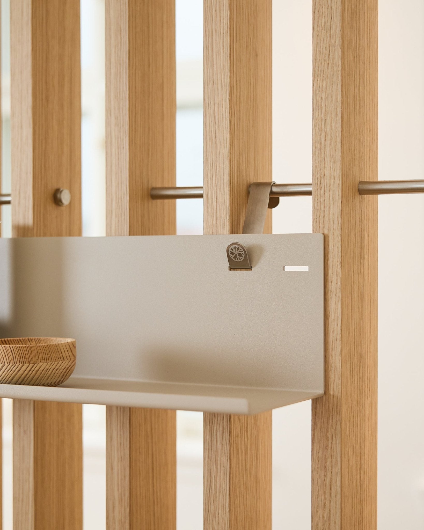 Beige Estante metálico WoodUpp BM1 Estantería (63x13,4 cm) montado en un panel acústico de lamas vertical, con un cuenco de madera en el lado izquierdo del estante.