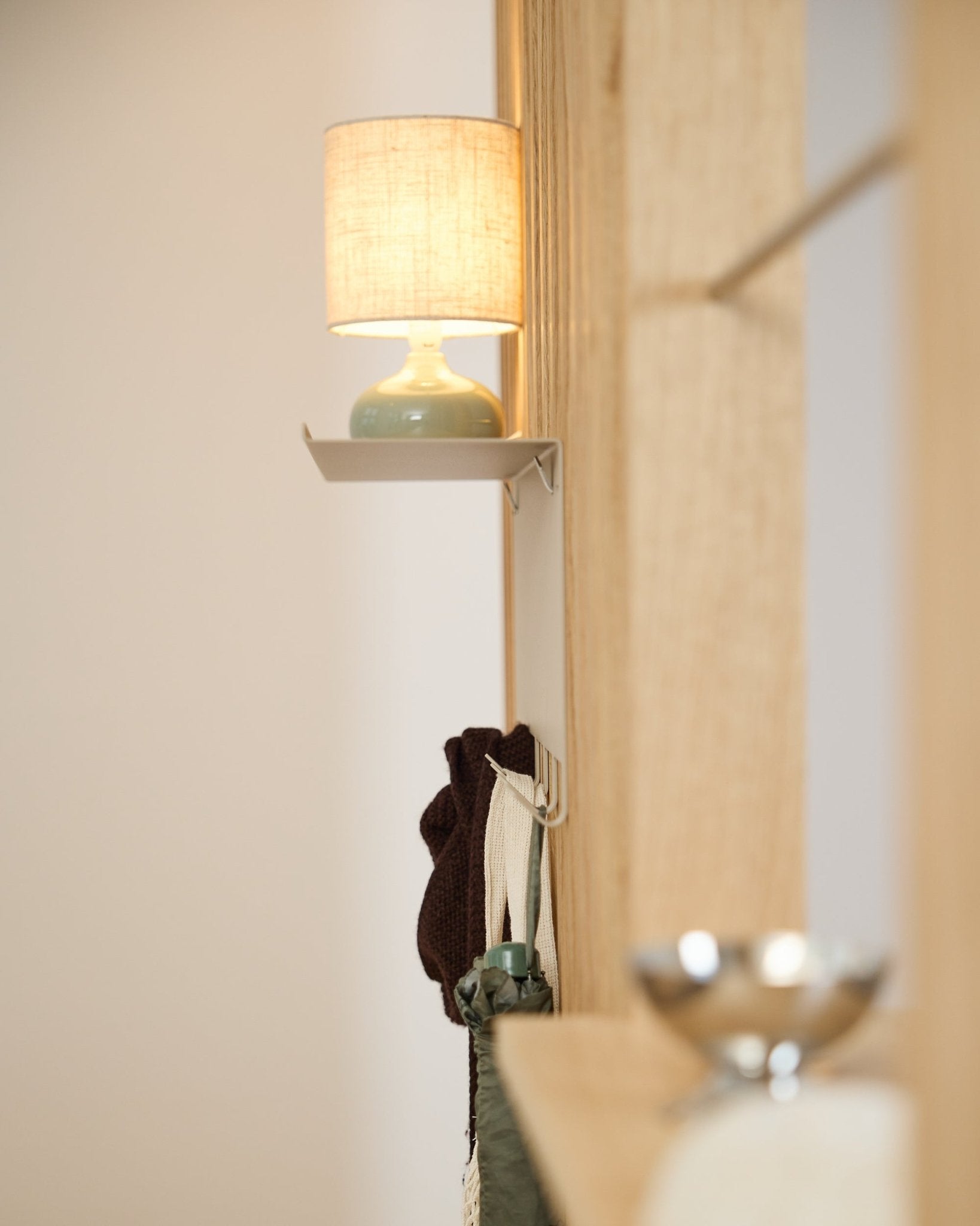 Un perchero WoodUpp Nell BM1 de beige (63,5 x 24 cm) se sitúa bajo una lámpara de mesa small, junto a una pared de madera nórdica clara Panel acústico.