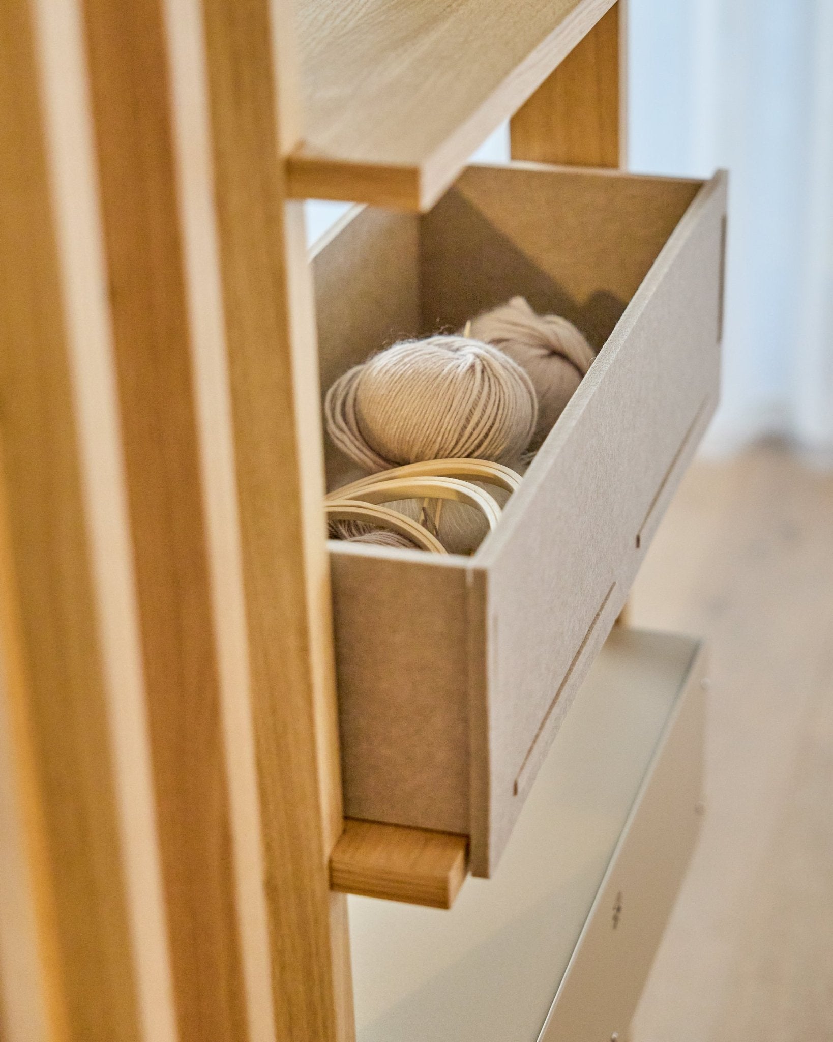 The WoodUpp Vigg Felt Box / BM2 en beige contiene ovillos ligeros y bastidores de bordado de madera sobre una estantería de madera, en armonía con los paneles acústicos nórdicos.