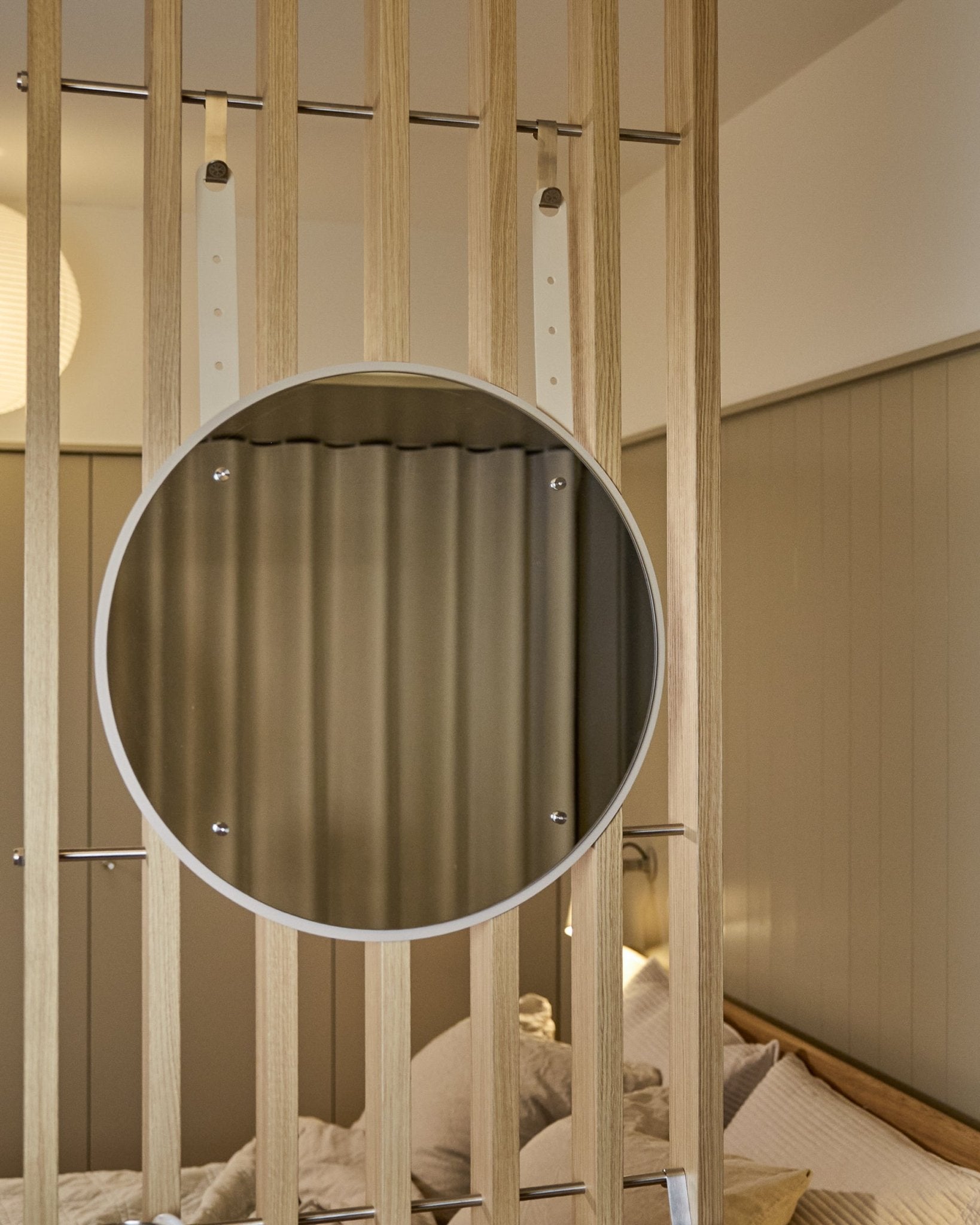 Espejo redondo Vala BM1 de altura ajustable de WoodUpp, 54 cm de diámetro, montado sobre vertical panel acústico de listones de madera con una iluminación suave en tonos neutros.