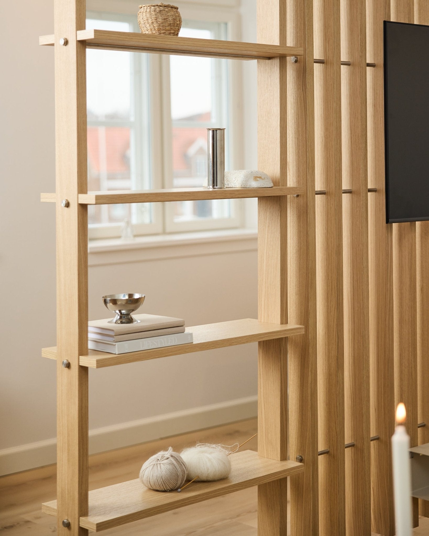 Separador de ambientes de roble claro de WoodUpp, con lamas vertical y estantes con libros y ovillos de lana.