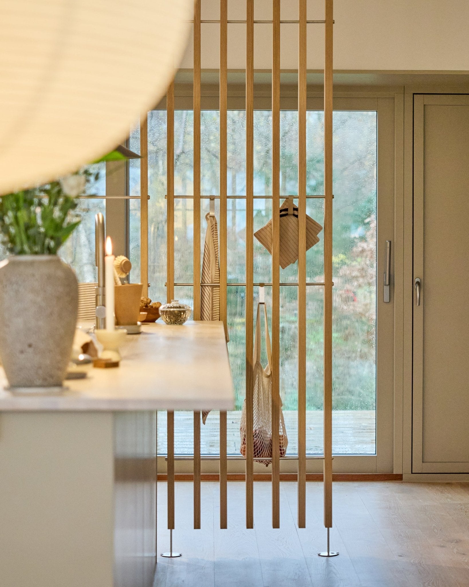 Cocina minimalista con un separador de ambientes WoodUpp Embrace (BM1, 286-302 cm) en chapa de roble, con encimeras claras, un jarrón con flores y vistas al jardín.