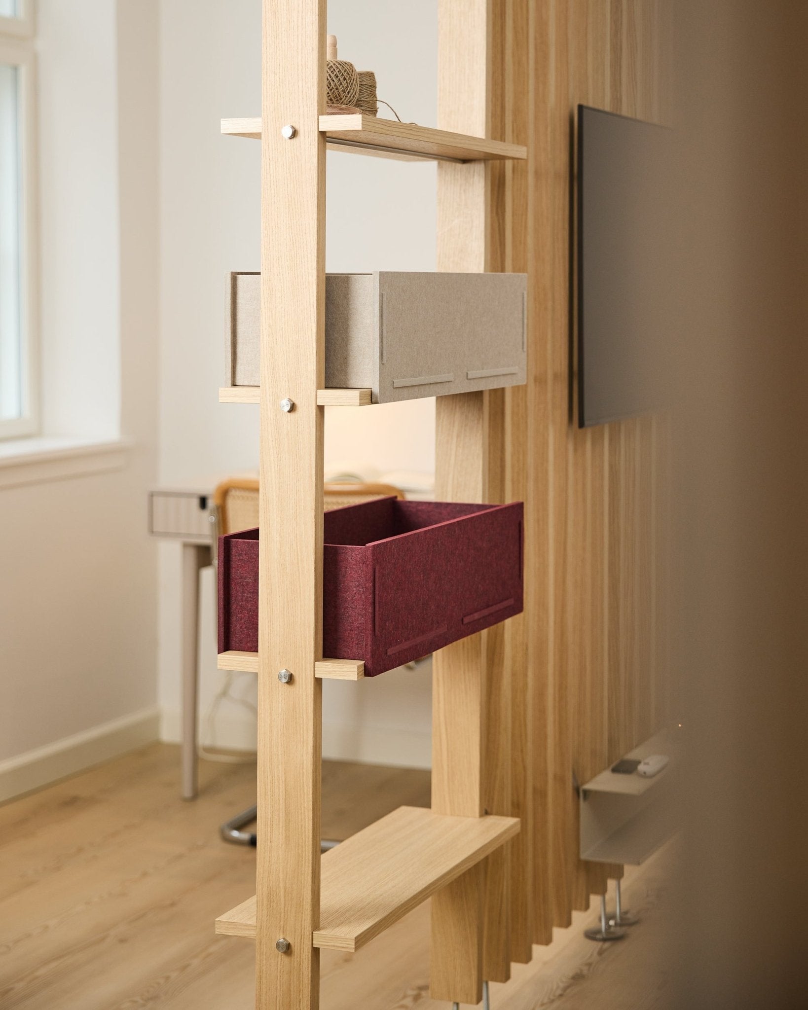 Una estantería de WoodUpp muestra una caja de almacenaje beige y una Vigg Felt Box / BM2 ox red en una estancia nórdica luminosa y minimalista con detalles acústicos de madera.