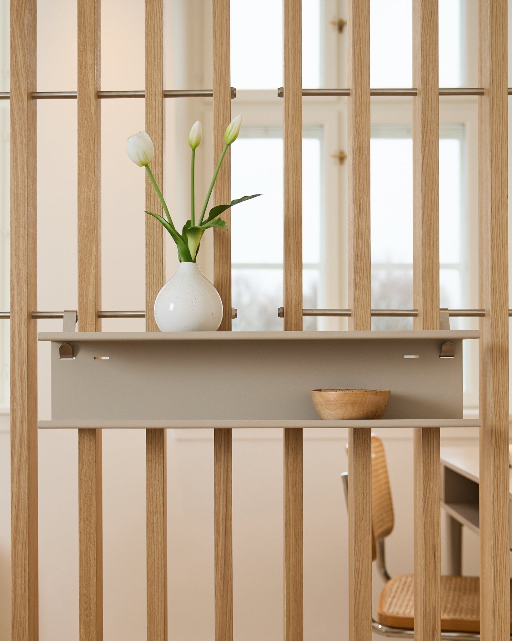 Double Metal Estantería/ BM1 de WoodUpp en beige (63,5 cm), montado en un separador de ambientes de listones y presentado con un jarrón y un cuenco de madera.