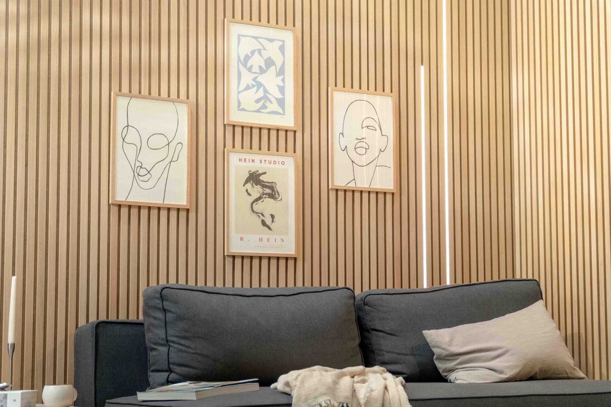 Moderno salón con un sofá oscuro con cojín beige, acentuado por una pared nórdica de listones de madera acústica Akupanel y arte minimalista escandinavo encima.