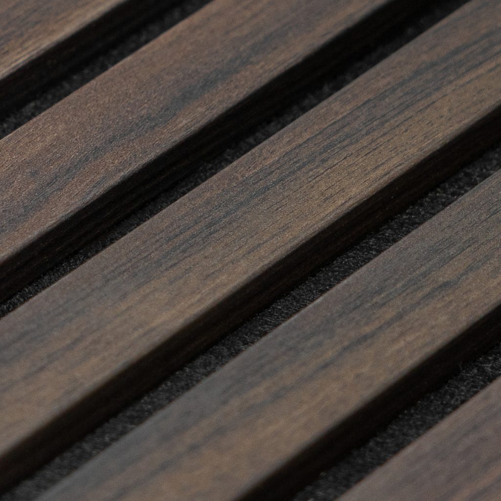 Panel acústico WoodUpp con lamas paralelas de madera en acabado nogal oscuro, veta visible y textura mate; lamas finas separadas por ranuras que muestran un respaldo negro texturizado. Diseño modular y elegante, pensado para revestimiento decorativo y control acústico en paredes o techos.