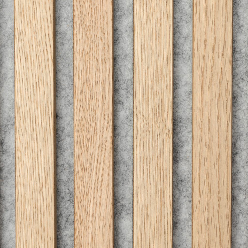 Panel WoodUpp con listones verticales de madera de roble claro: cuatro listones lisos con veta visible, colocados en paralelo sobre un respaldo gris de fieltro acústico, mostrando la textura de la madera y las ranuras que permiten absorción sonora y diseño estético.