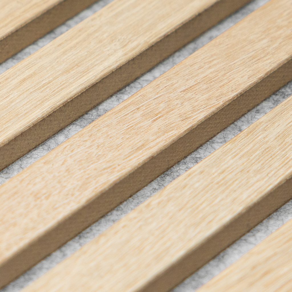 Primer plano de listones de madera natural WoodUpp dispuestos en paralelo sobre un respaldo acústico blanco. Se aprecian superficies de roble claro con cantos rectos y el tejido fieltro gris-blanco entre las ranuras, detalle texturado del panel acústico modular WoodUpp.