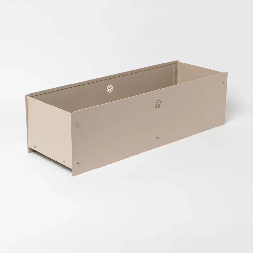 Macetero rectangular modular metálico de WoodUpp en color beige, diseñado como cajón alto para cultivo o jardinería interior/exterior; paneles remachados con pequeños orificios decorativos en forma de flor, esquinas en ángulo y acabado mate, sin plantas ni tierra, con tornillería plateada visible y fondo elevado.