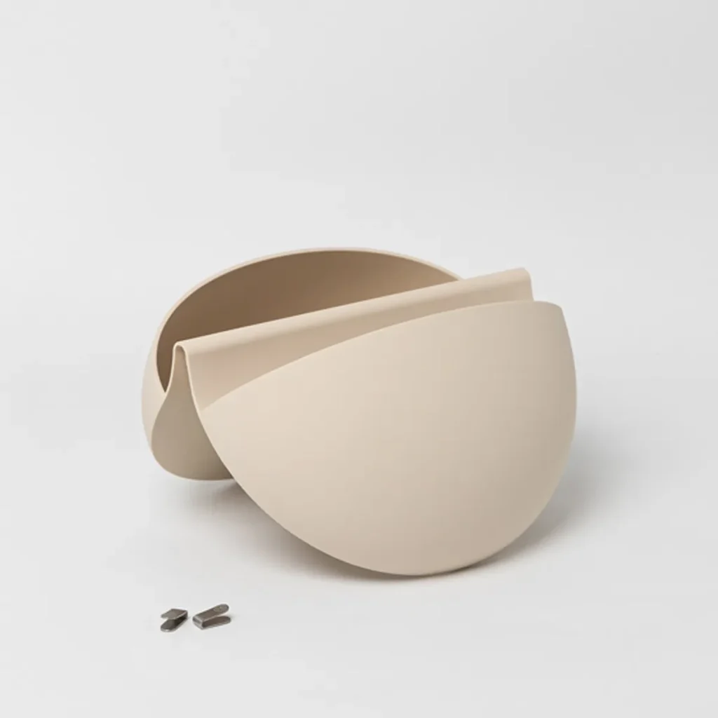 Imagen de dos maceteros colgantes modulares beige de WoodUpp, en forma de semiesfera con apertura frontal y diseño curvo superpuesto, acompañados por tres pequeñas piezas metálicas de montaje. Presentación minimalista sobre fondo blanco, mostrando textura lisa y líneas orgánicas del producto.