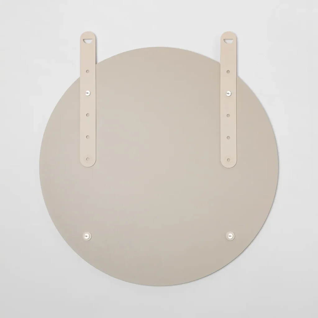 Espejo redondo de WoodUpp visto desde atrás, con acabado beige mate y superficie lisa, dos correas verticales regulables tipo cuero con orificios y remaches, herrajes y tornillos metálicos plateados para colgar, además de dos puntos de fijación inferiores; diseño minimalista y montaje sencillo.