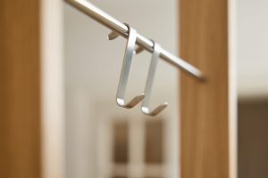 Ganchos colgadores WoodUpp de aluminio cepillado, diseño en U delgado y minimalista, colgados en una barra metálica dentro de un armario; se aprecian dos unidades con acabado plateado y protectores circulares en las puntas, ideales para bolsos, cinturones o ropa.